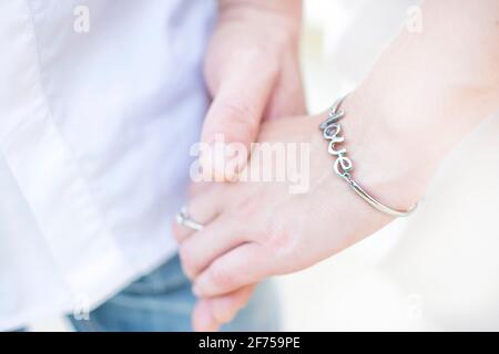primo piano della mano di un uomo che tiene una mano di una donna dentro un bracciale con l'iscrizione amore Foto Stock