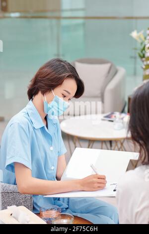 Il documento di riempimento di un giovane infermiere medico serio durante l'ascolto dei reclami di paziente di sesso femminile Foto Stock