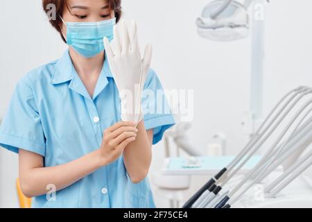 Immagine ritagliata di infermiere medico in maschera protettiva che si mette su guanto in silicone pronto per curare il paziente Foto Stock