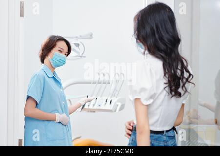Infermiere positivo in maschera medica invitando giovane paziente femminile in ufficio di dentista Foto Stock
