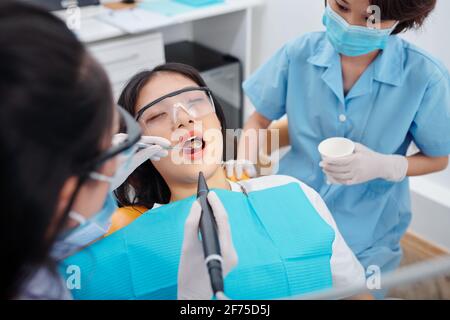 Dentista che fora i denti di giovane paziente femminile che soffre di teethache Foto Stock