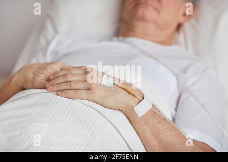 Primo piano di un uomo anziano irriconoscibile sdraiato sul letto dell'ospedale con l'ago flebo in mano, spazio per la copia Foto Stock