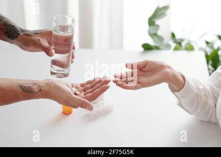 Mani dell'uomo che danno un bicchiere d'acqua e pillole o. supplementi a sua madre anziana Foto Stock