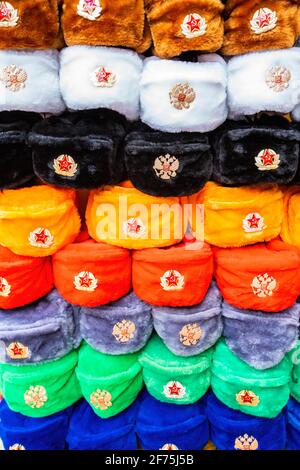Mosca, Russia - 4 aprile 2021: File di cappelli invernali russi di diversi colori con emblemi dell'esercito al mercato di strada in Old Arbat Street, iconico popolare souvenir russo. Foto di alta qualità Foto Stock