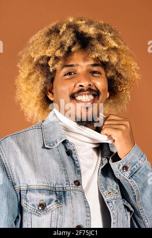 Foto di scorta di un allegro uomo afro sorridente e guardando la fotocamera in studio girato su sfondo marrone. Foto Stock