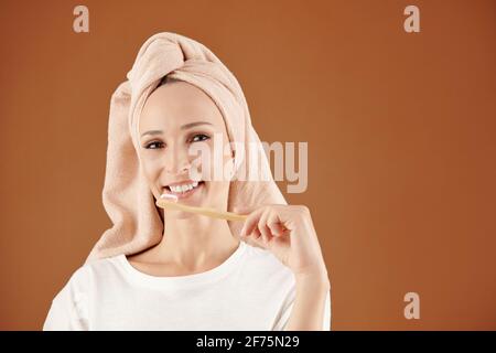 Ritratto di giovane donna sorridente che sfrega i denti con legno spazzola dopo la doccia Foto Stock