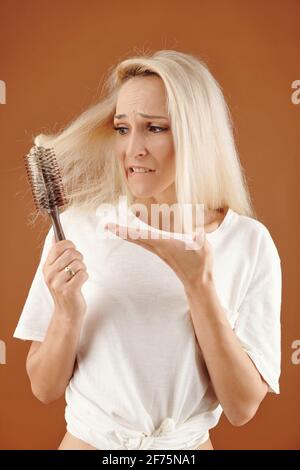 Giovane donna infelice con i suoi capelli biondi secchi tinti aggrovigliati nel pennello Foto Stock