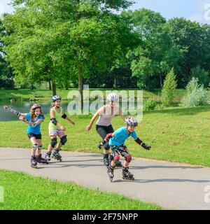 Giovane famiglia facendo un tour sui pattini inline nel parco urbano in un pomeriggio di sole in estate Foto Stock