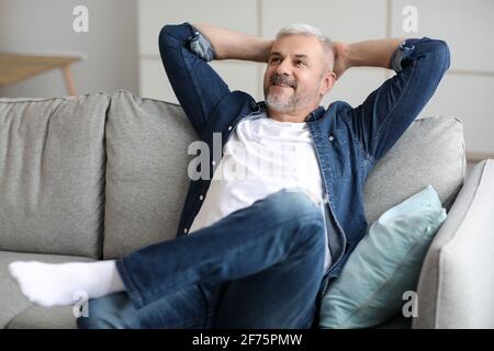 Felice uomo anziano sopportato che si rilassa sul divano a casa Foto Stock