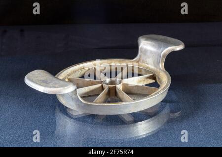 Un vecchio taglierino di mela di metallo su un tavolo di vetro con un riflesso. Utensili da cucina su sfondo nero Foto Stock