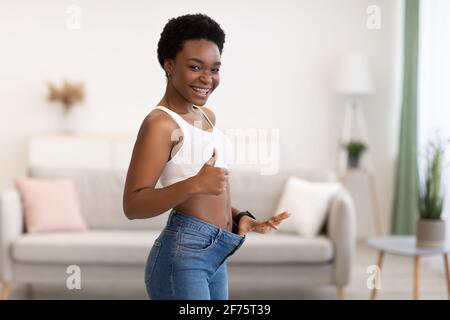 Slim Black Lady che mostra il risultato di una gesturing dimagrante come in interni Foto Stock