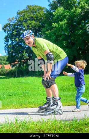 L'uomo facendo un tour di pattinaggio su pattini a rotelle in linea con l'aiuto del suo piccolo figlio nel verde della natura Foto Stock