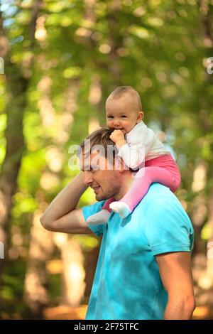 Il bambino si siede sulle spalle dei suoi padri. Padre e bambino che camminano nel parco. Ora legale. Buona famiglia. Foto Stock