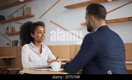 sorridente partner di affari interrazziali che parlano durante la riunione in caffetteria Foto Stock