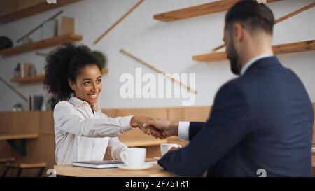 felici soci di affari interrazziali che scuotono le mani durante la riunione nel caffè Foto Stock