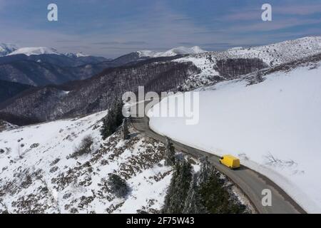 Immagine aerea di un carrello a microbus giallo in movimento su a. strada di montagna innevata Foto Stock