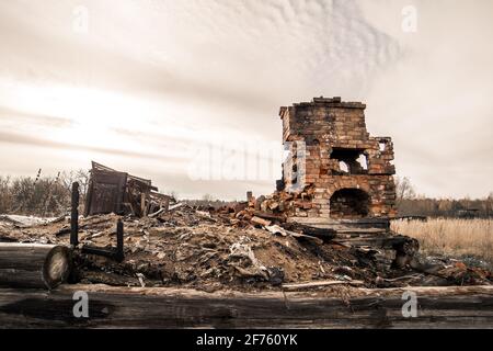 Una stufa di riscaldamento distrutta che sta in piedi da solo in un lotto vacante. Casa bruciata a terra dopo il fuoco. Sullo sfondo c'è un cielo grigio cupo. Un quadro tragico che crea anelito e solitudine. Foto Stock