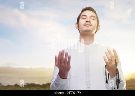 Uomo musulmano asiatico che prega con perle di preghiera sulle sue mani con sfondo blu Foto Stock