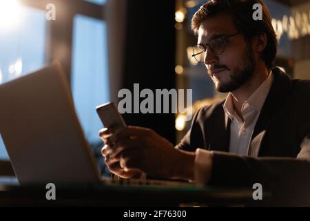 Bel giovane uomo d'affari che lavora su un computer portatile alla scrivania dell'ufficio fino a tarda notte. Foto Stock