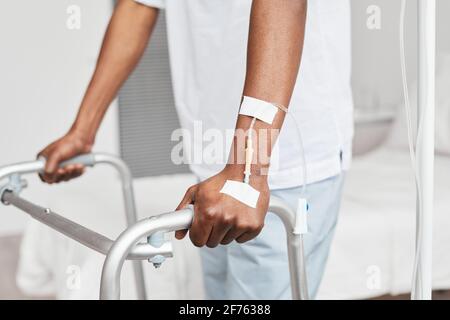 Primo piano di un uomo afroamericano irriconoscibile che si appoggia sul camminatore in ospedale, concentrarsi sul catetere fleboclisi iv in mano, copiare spazio Foto Stock