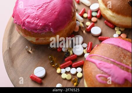 Malsano e dolci. Ciambelle e pillole smaltate su piastra di legno. Foto di alta qualità Foto Stock