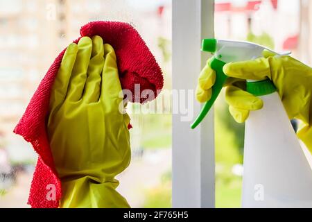 Lavaggio delle finestre e pulizia della casa. La governante in guanti gialli lava e pulisce il vetro sporco. Foto Stock