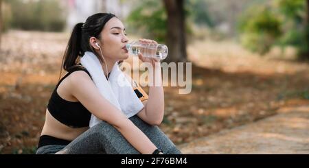 La giovane atleta prende una pausa, acqua potabile, fuori su una corsa in una giornata calda. Foto Stock