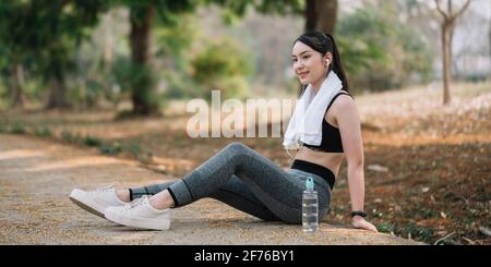 Donna asiatica atletica che riposa dopo un duro allenamento in montagna al tramonto. Abiti sportivi stretti Foto Stock