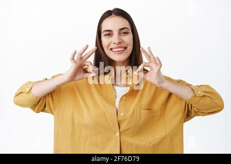 Molto bene, sì. Sorridente donna caucasica mostra segni OK, fare un gesto OK per approvare, d'accordo o come qualcosa di buono, lodare scelta eccellente, ben fatto Foto Stock