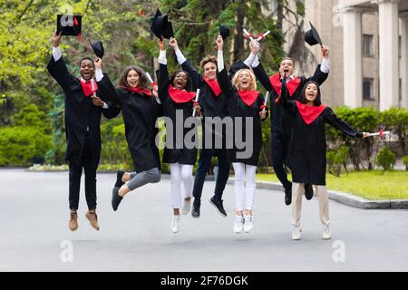 Felici studenti che festeggiano la laurea dall'università, saltando in su Foto Stock