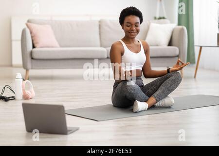 Donna afroamericana meditando al laptop facendo yoga a casa Foto Stock