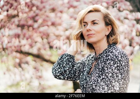 Ritratto di una bella donna negli anni '40. Profilo ritratto con un albero di magnolia fiorito rosa come sfondo. Sicuro eccellente donna aggraziata. Foto Stock