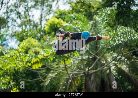 Uomo freestyle estremo rollerblading alto in aria con pattini in linea e casco al Parco Municipale di Mangabeiras, Belo Horizonte, Brasile Foto Stock