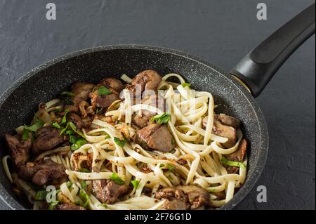 Fegato di pollo cotto con cipolla e spaghetti su una penna da cucina con prezzemolo. Gustosa cena di famiglia. Foto Stock