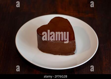 Torta al cioccolato a forma di cuore su piatto su sfondo di legno scuro Foto Stock