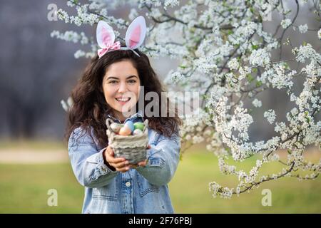 Felice giovane donna che indossa coniglietto orecchie che tiene colorate uova di pasqua Foto Stock
