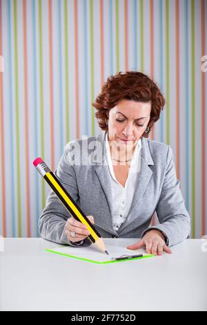 Donna d'affari che scrive con una matita gigante al suo ufficio Foto Stock