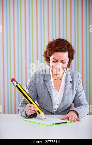 Donna d'affari che scrive con una matita gigante al suo ufficio Foto Stock