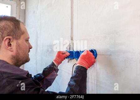 L'elettricista inserisce la scatola di plastica direttamente nei fori di uscita. Primo piano Foto Stock