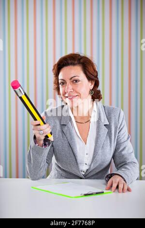 Donna d'affari che scrive con una matita gigante al suo ufficio Foto Stock