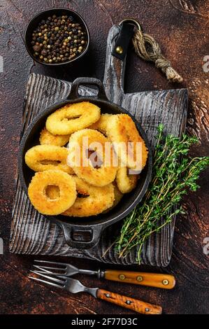 Anelli di calamari fritti impanati su un tagliere. Sfondo scuro. Vista dall'alto. Foto Stock