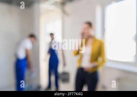 Sfondo offuscato di costruttori stanno rinnovando una stanza, una donna parla al telefono. Foto Stock