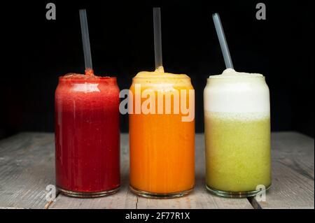 Tre bicchieri di succhi freschi colorati con cannucce di plastica. Concetto di dieta di barbabietola, arancia e succo verde Foto Stock