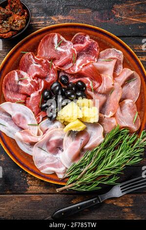 Piatto di carne italiana con prosciutto, bresaola, pancetta, salame e parmigiano. Sfondo di legno scuro. Vista dall'alto Foto Stock