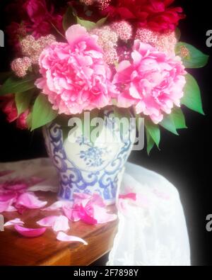 BOUQUET ANNI '90 DI PEONIE ROSA E ROSSO IN BLU E. PETALI DI VASO BIANCHI CHE CADONO SU TAVOLA DI LEGNO - KF30634 PET001 HARS VECCHIO STILE Foto Stock