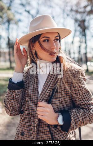 Bella donna che indossa blazer elegante, cappello che tiene borsa nel parco. Primavera femminile outfit alla moda. Primo piano Foto Stock