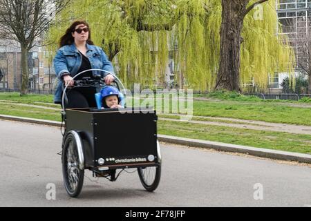 Giovane madre e suo bambino che cavalcano in una bici da carico nel parco di Londra, Inghilterra Regno Unito Regno Unito Foto Stock