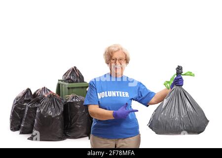 Donna anziana volontaria che indica un sacchetto di rifiuti davanti di un contenitore isolato su sfondo bianco Foto Stock