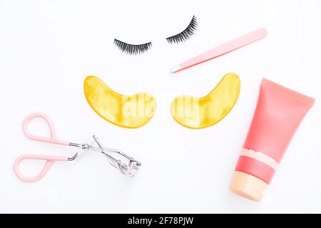 Strumenti e false ciglia con macchie dorate su sfondo bianco. La vista dall'alto. Foto Stock