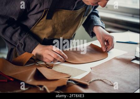 Un giovane ragazzo di talento aiuta suo padre nel commercio di famiglia, taglia fuori gli sbozzi per le scarpe dalla pelle. Foto Stock